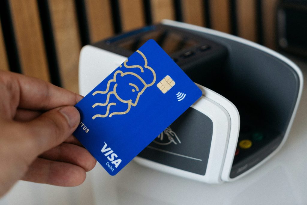 A hand holding a blue Visa card near a payment terminal for a tap payment