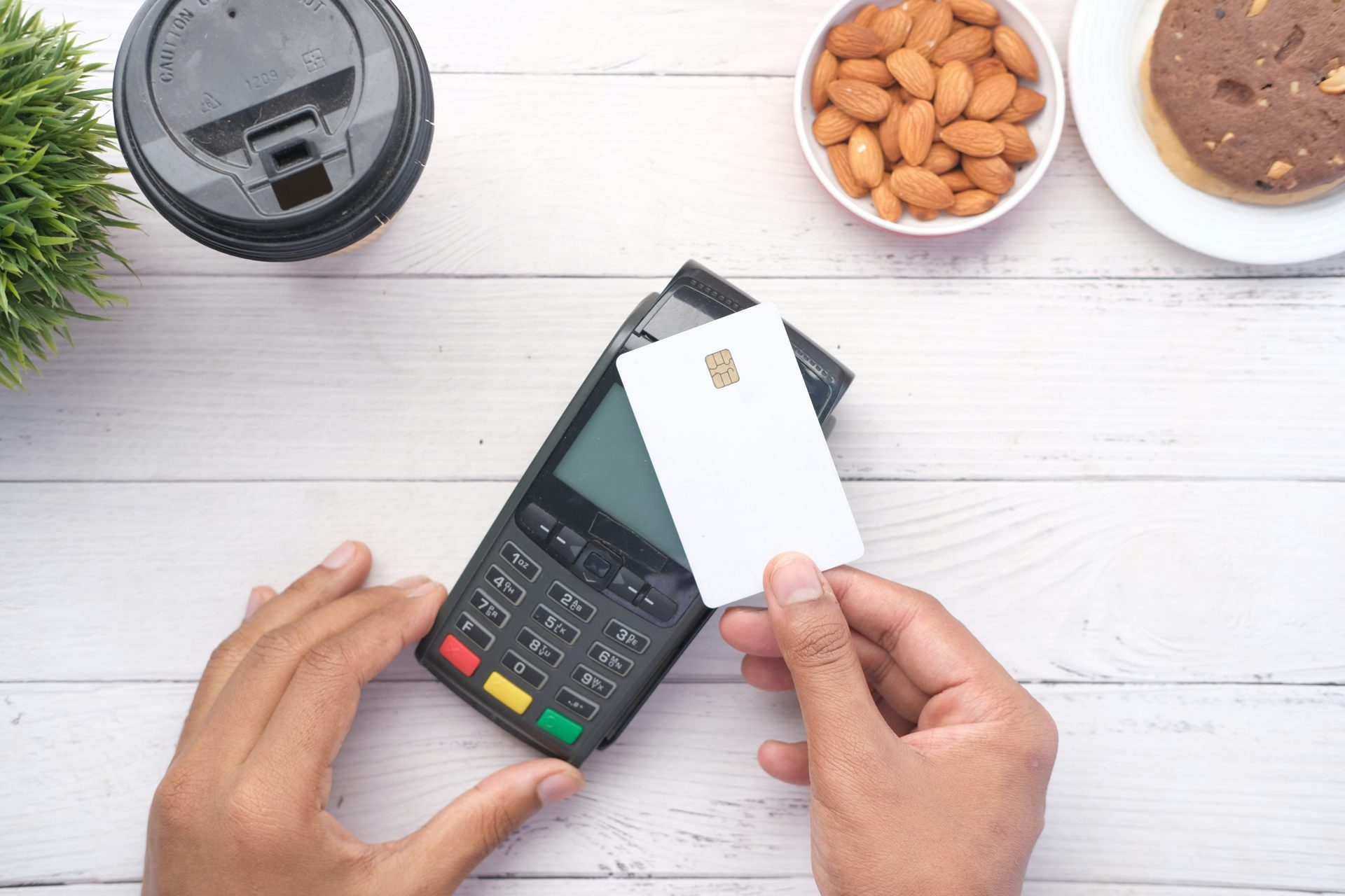 A person tapping a card on a payment terminal next to a coffee cup and snacks